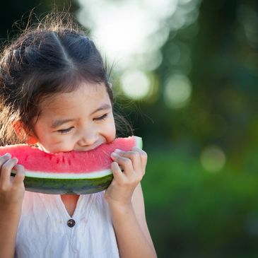 Cute asian little child girl eating watermelon fresh fruit in the garden